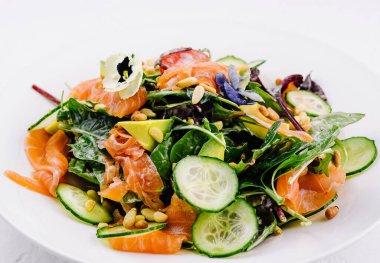 Gourmet somon salatası, karışık yeşillikler, salatalık dilimleri ve çekirdekler, kıtır beyaz arka planda servis edilir.