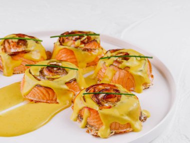 Beyaz bir tabakta, bitkilerle süslenmiş kremalı hollandaise ile nefis somon ısırıkları.