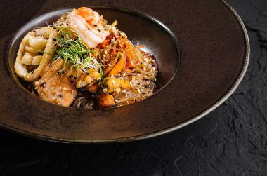 Pürüzsüz bir tabakta servis edilen karides ve otlu deniz ürünleri makarnasının zarif bir sunumu.