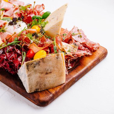 İçinde çeşitli peynirler, pişirilmiş etler ve ahşap bir yüzey üzerindeki süslerin bulunduğu zarif şarküteri tahtası.