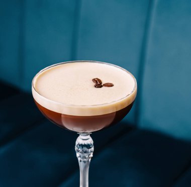 Kahve çekirdeği garnitürlü espresso martini, beyaz bir masada mavi bir arkaplanda servis edilir.