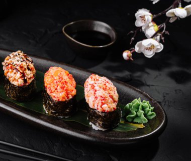 Suşi rulo çeşitleri geleneksel aksesuarlarla birlikte parlak siyah bir levhada servis edilir.