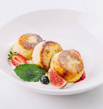 Çilek ve nane şekeriyle süslenmiş üç altın rengi süzme peynir krepi.