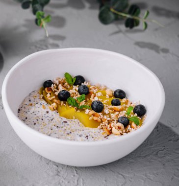 Besleyici chia tohumu pudingi meyvelerle süslenmiş, fındıklar gri bir yüzeyde.