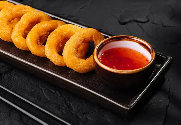 Golden-brown onion rings served on a slate tray with spicy dip and chopsticks, elegant food presentation