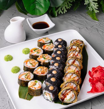 Soya soslu, wasabi soslu ve zencefilli turşulu beyaz bir tabakta servis edilen taze suşi ruloları.