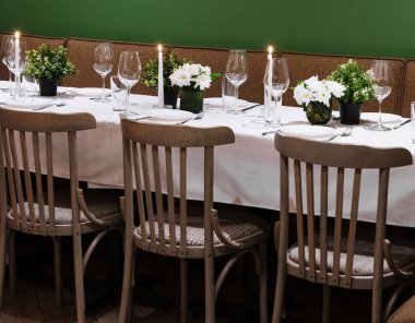 Yeşil bir duvara karşı mumlar, çiçekler ve şarap kadehleriyle hazırlanmış rahat bir restoran masası.