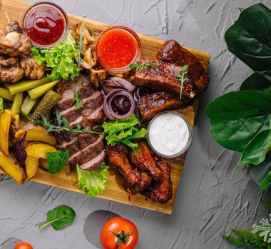 Tahtaya batırılmış taze malzemelerle çevrili nefis bir bbq ziyafetinin üst görüntüsü.