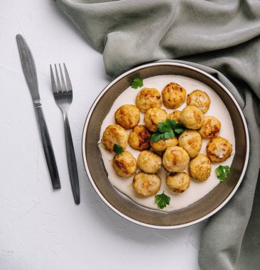 Krema soslu ev yapımı köfteler seramik tabakta maydanoz, çatal bıçak ve peçete.