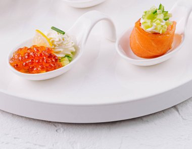 Beyaz seramik tabakta gurme somon ve parlak arka planda havyar aperatifleri.