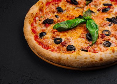 Siyah zeytin ve koyu arkaplanda taze fesleğenle süslenmiş iştah açıcı peynirli pizza.