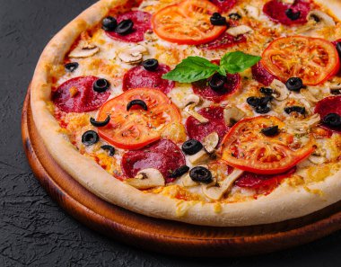 Koyu arkaplanda malzemeler olan yeni pişmiş bir pizzanın yakın çekimi.