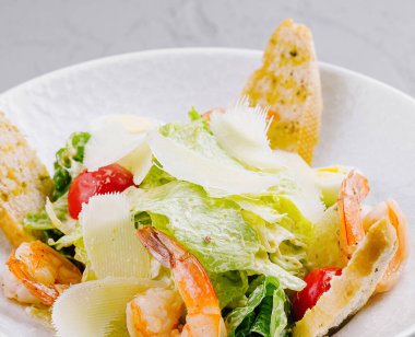 Lezzetli karides, tıraşlı parmesan ve beyaz tabakta altın kıtır ekmek ile iştah açıcı sezar salatası