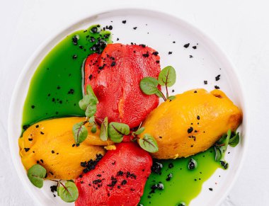 Izgara kırmızı ve sarı dolma biber baharatlı otlar ve beyaz bir tabakta yağ.