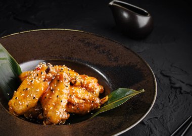 Yeşil yapraklarla süslenmiş, nefis, siyah bir tabakta servis edilen susamlı teriyaki tavuğu.