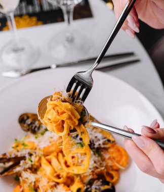 Güzel bir yemek ortamında deniz mahsullü makarna ile çatal çeviren birinin yakın çekimi.