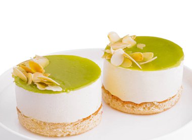 Beyaz bir tabakta badem dilimli iki ayrı limonlu cheesecake, beyaz arka planda izole edilmiş.
