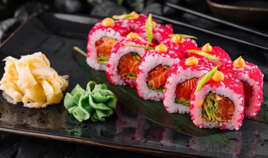 Yanında wasabi ve zencefil ile birlikte siyah bir tabakta balık yumurtası ile süslenmiş nefis suşi ruloları.