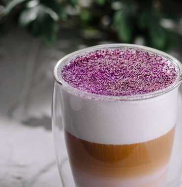 Açık bir fincanda mor köpüklü, yeşil desenli gri bir yüzey üzerine modadan katmanlı latte.