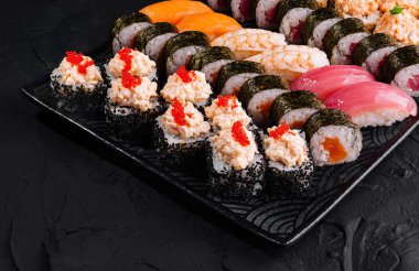 Japon mutfağı konsepti için mükemmel siyah bir levhada servis edilen lezzetli suşi ruloları.