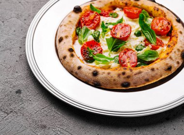 Lezzetli margherita pizza, domatesli ve fesleğenli, beyaz tabakta, siyah arka planda