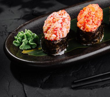 Suşi rulo çeşitleri geleneksel aksesuarlarla birlikte parlak siyah bir levhada servis edilir.