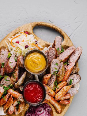 Ahşap servis tahtasının üstünde ızgara sosis, sos ve süslemeler var.