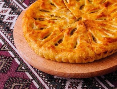 Yeni pişmiş Gürcü peynirli ekmek, Khachapuri, etnik desenli bir geçmişe sahip ahşap bir tahtada servis ediliyor.