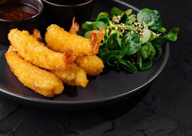 Taze salatayla servis edilen gurme karides ve iki soslu siyah tabak.