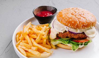 Altın patates kızartması ve beyaz tabakta ketçap ile servis edilen sulu çizburger.