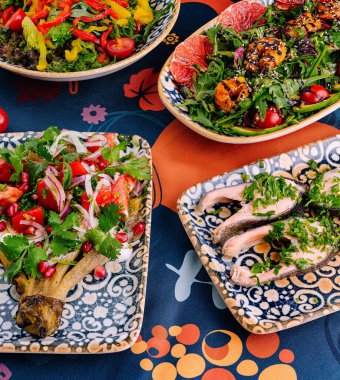 Arkaplanda taze malzemelerle desenli bir masa örtüsü üzerinde dekoratif kâselerde servis edilen canlı Akdeniz mutfağı.