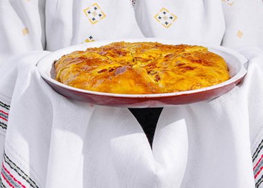 Halk kostümü giyen kişi ev yapımı bir turta tutuyor. Kültürel mutfağı gösteriyor.