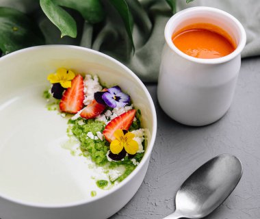 Şam fıstığı yeşili granola, canlı yenilebilir çiçekler ve taze çilek dilimleri ile zarif bir kahvaltı kasesi.