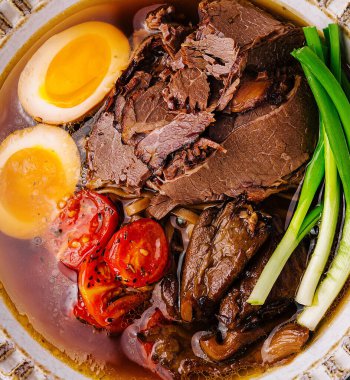 Geleneksel sığır etli ramen, yumuşak yumurta, domates ve yeşil soğan.