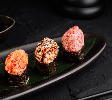 Suşi rulo çeşitleri geleneksel aksesuarlarla birlikte parlak siyah bir levhada servis edilir.