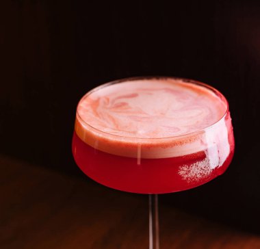 Süslü, köpüklü kırmızı bir kokteyl, klasik bir kök bardakta servis ediliyor.
