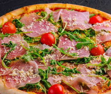 Prosciutto, vişneli domates, roka ve parmesanlı taze pişmiş pizza.