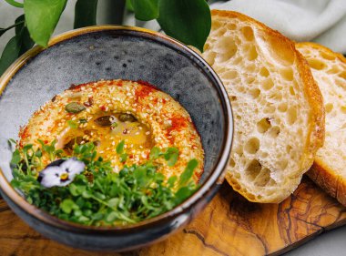 Tohumlarla süslenmiş bir kase kremalı humus ve taze zanaatkar ekmeğiyle servis edilen canlı bir yenilebilir çiçek.