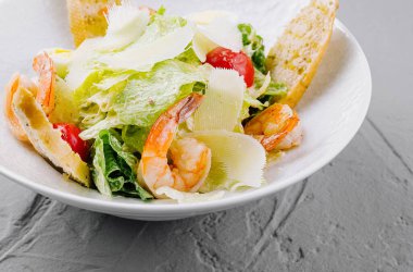 Lezzetli karides, tıraşlı parmesan ve beyaz tabakta altın kıtır ekmek ile iştah açıcı sezar salatası