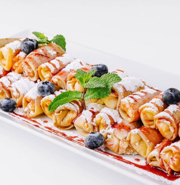 Şerbetle sulandırılmış, toz şekerle tozlanmış taze böğürtlen ve nane yapraklarıyla süslenmiş enfes mini krepler.