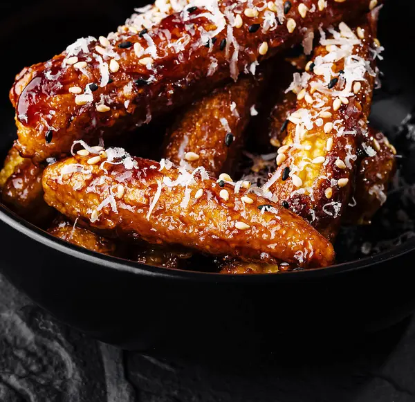 stock image Sweet and savory honey glazed chicken wings with sesame seeds in a stylish black bowl