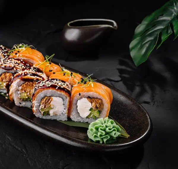 Nefis bir suşi rulosu sunuldu. Yanında yemek çubukları olan siyah, şık bir tabakta servis edildi.