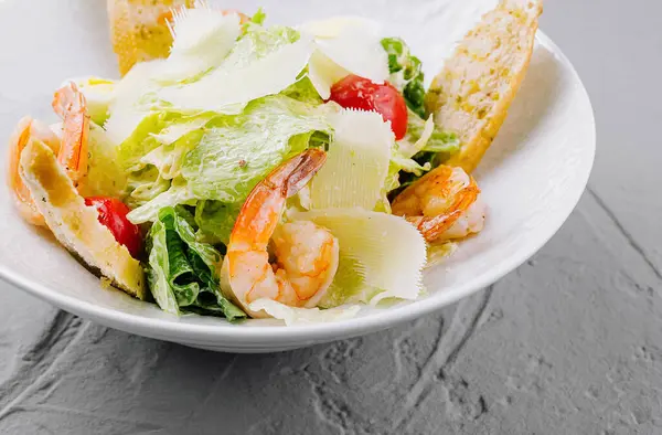 Lezzetli karides, tıraşlı parmesan ve beyaz tabakta altın kıtır ekmek ile iştah açıcı sezar salatası