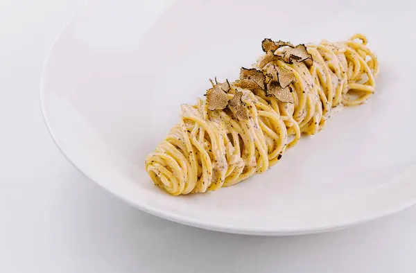 stock image Elegant serving of spaghetti topped with shaved truffles on a sleek plate, marble background