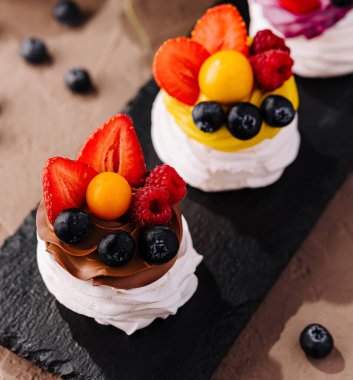 Üç mini pavlovas, çırpılmış krema ve taze böğürtlen servis tahtasında.
