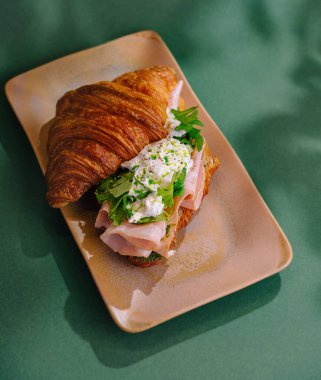 Jambonlu, peynirli ve yeşillikli taze kruvasan sandviçi, şık bir tabakta servis edilir.
