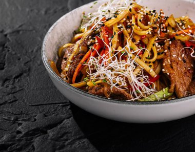 Makarna, renkli sebzeler ve bir kasede susam tohumlu tuzlu biftek.