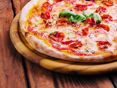 Fesleğenli pizza, kırmızı soğan ve ahşap bir tahtada sosis yakın plan.