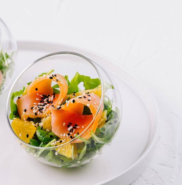 Şık cam kaselerde servis edilen sağlıklı füme somon salatası, karışık yeşiller ve susam tohumları.