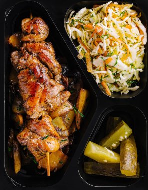 Sağlıklı ızgara tavuk yemeği, yanında lahana salatası ve turşu ve siyah bir kabın içinde.